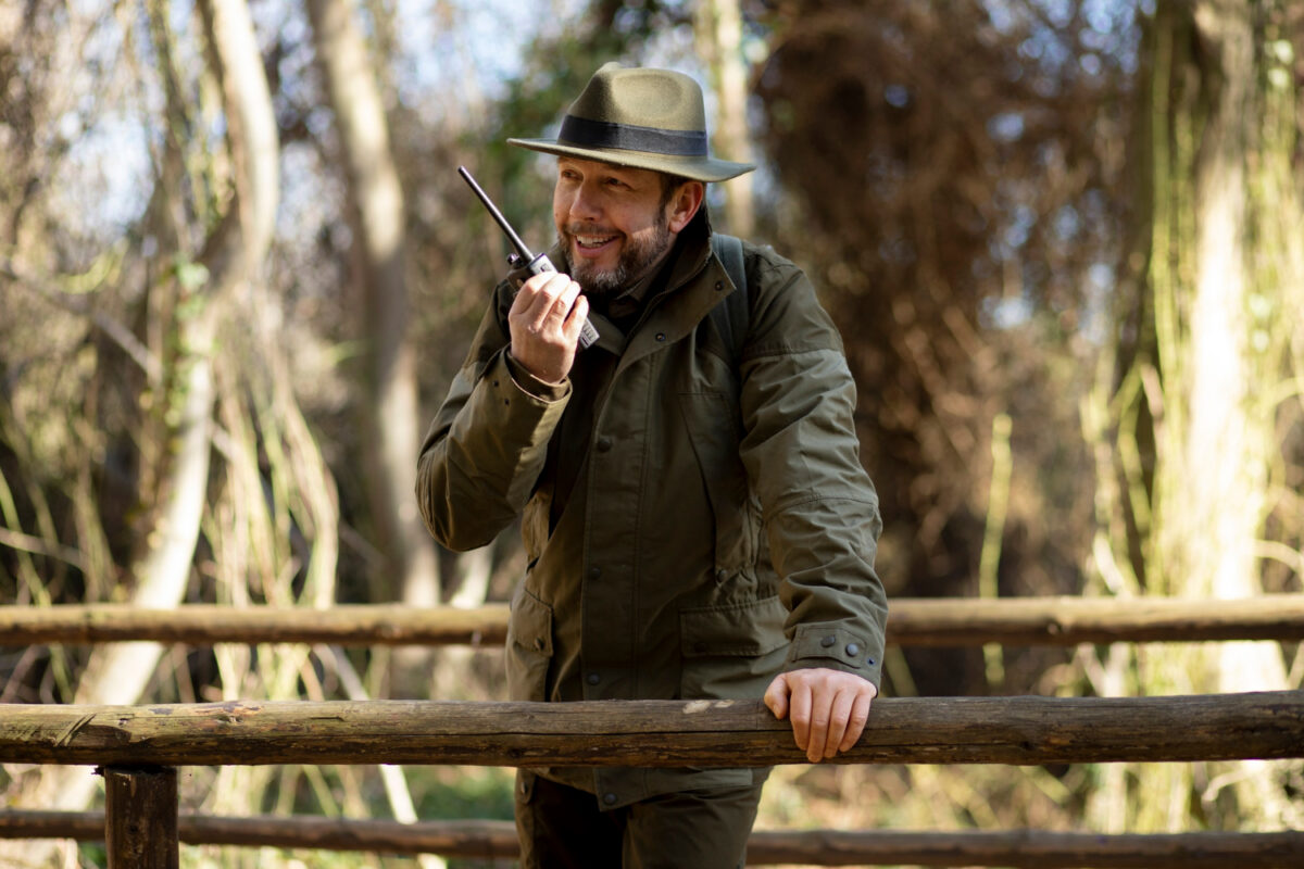 Gros plan sur un chasseur dans les bois avec un talkie walkie à la main.